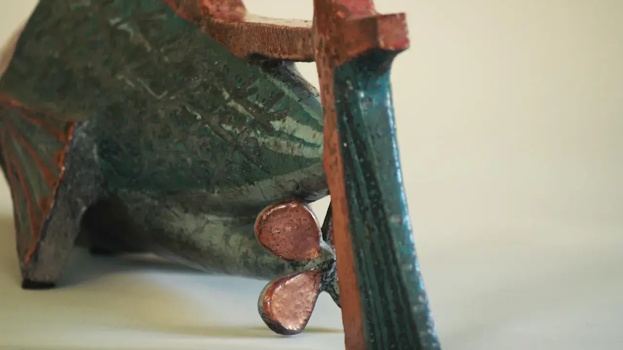 Sculpture de poisson en céramique, style Jean Derval, aux couleurs vives bleu-vert et rouge, avec une hélice visible.