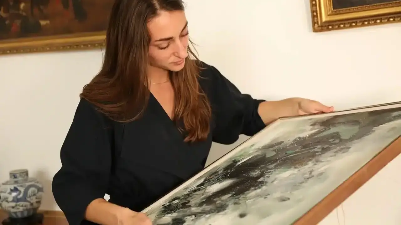 Une femme examine un tableau abstrait, cherchant des indices pour comment estimer un tableau avec signature.
