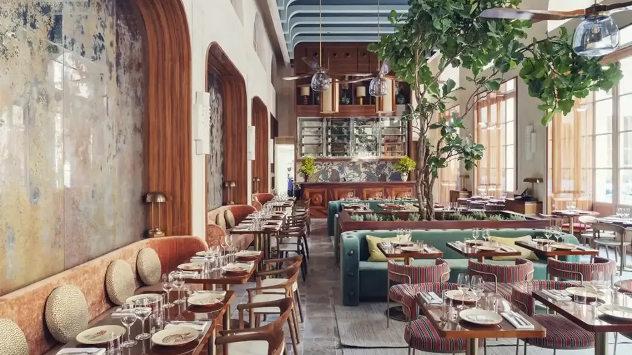 Intérieur d'un restaurant au style restauration architecture, avec banquettes velours, tables dressées et un arbre luxuriant au centre.