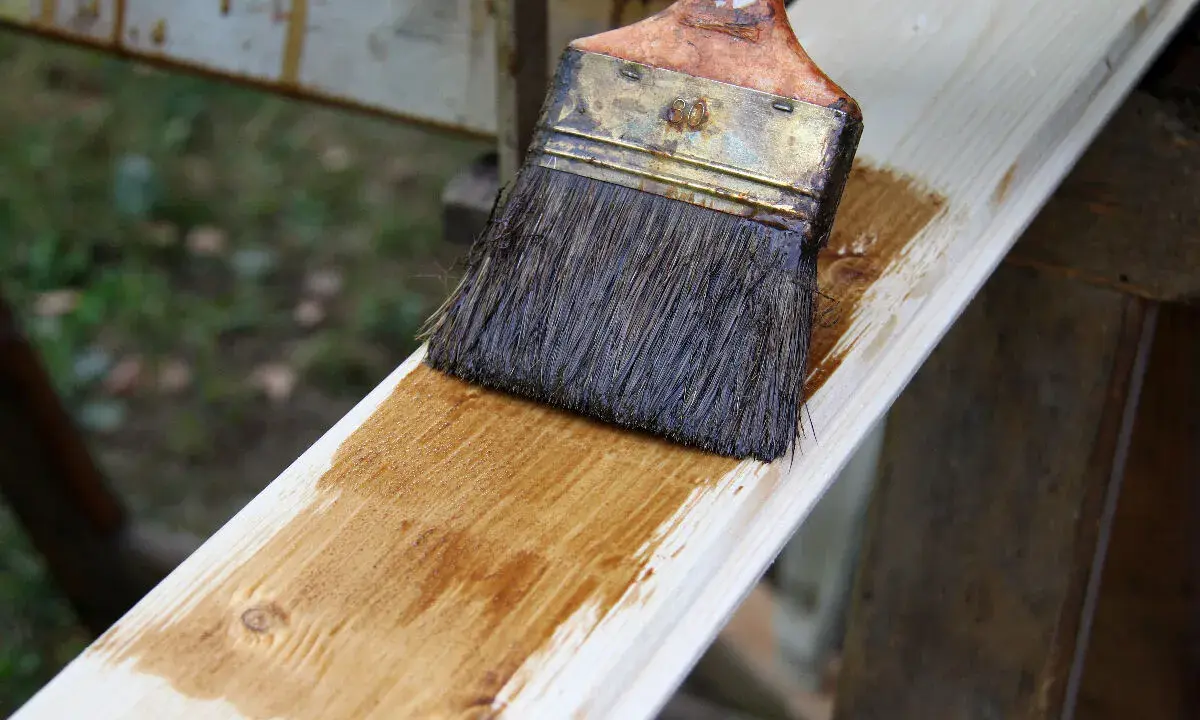 Pinceau appliquant une lasure sur une planche de bois clair, montrant la facilité de lasurer sans poncer pour une finition rapide et efficace.