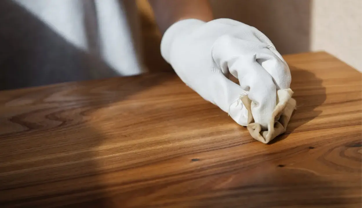 Main d'une personne portant un gant blanc, cirant un meuble en bois après décapage. La cire donne un éclat subtil au bois.