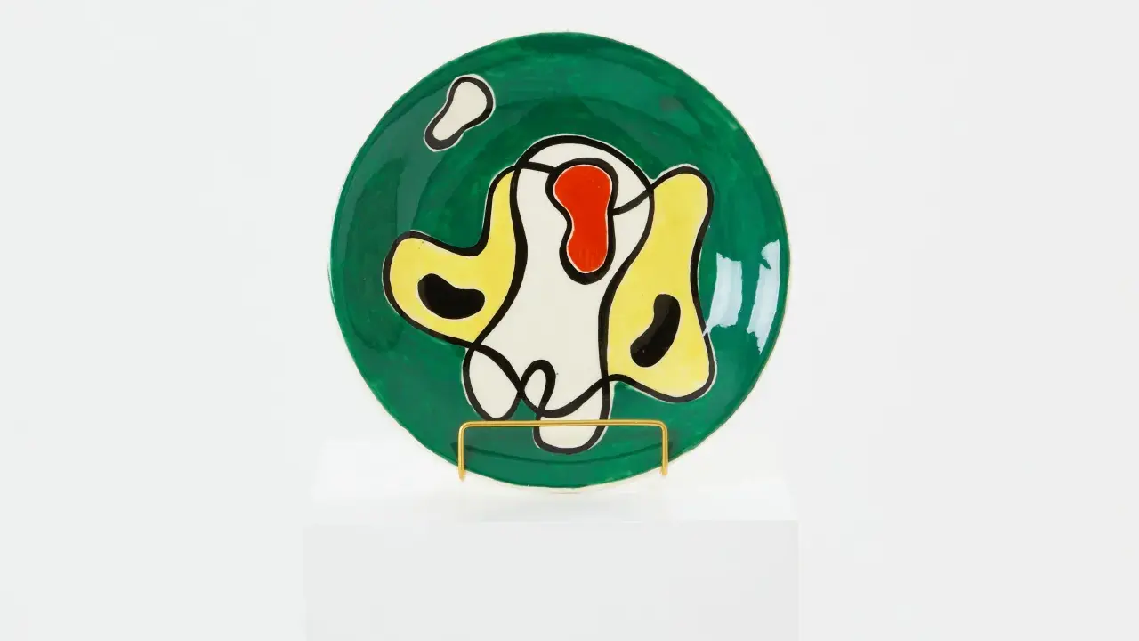 Assiette ronde verte ornée de formes abstraites noires, jaunes, rouges et blanches, dans le style de Roland Brice.