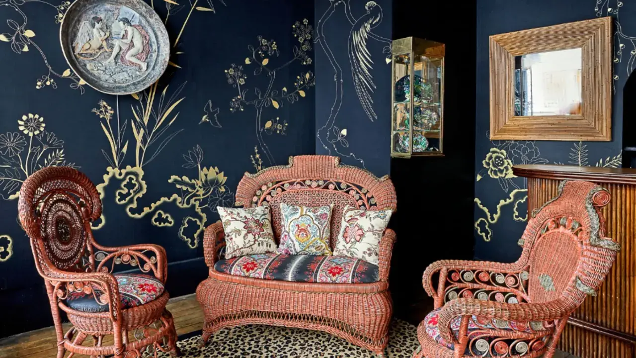 Salon au style napoléon 3, avec des fauteuils et un canapé en rotin corail, sur un tapis léopard, devant un papier peint bleu nuit orné de motifs dorés.