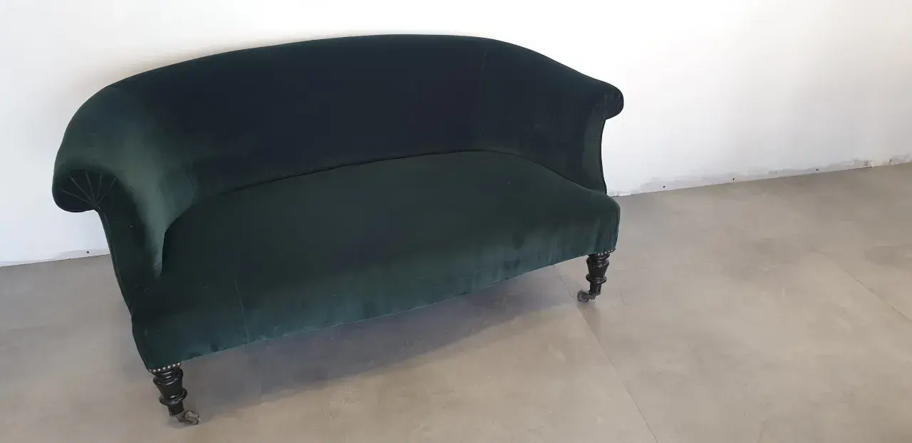Banquette Napoléon III en velours vert profond, aux pieds sculptés et roulettes. Un meuble élégant pour un salon d'époque.