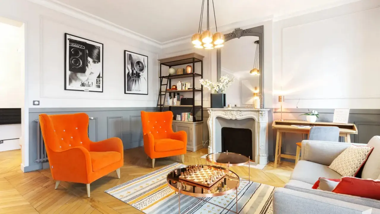 Salon aux fauteuils orange vif, cheminée ornée, et un jeu d'échecs sur table basse, évoquant un mouvement baroque moderne.