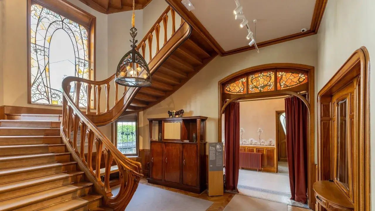Escalier majestueux en bois, vitraux colorés, mobilier ancien. Un intérieur d'une élégance intemporelle, évoquant le style Majorelle.