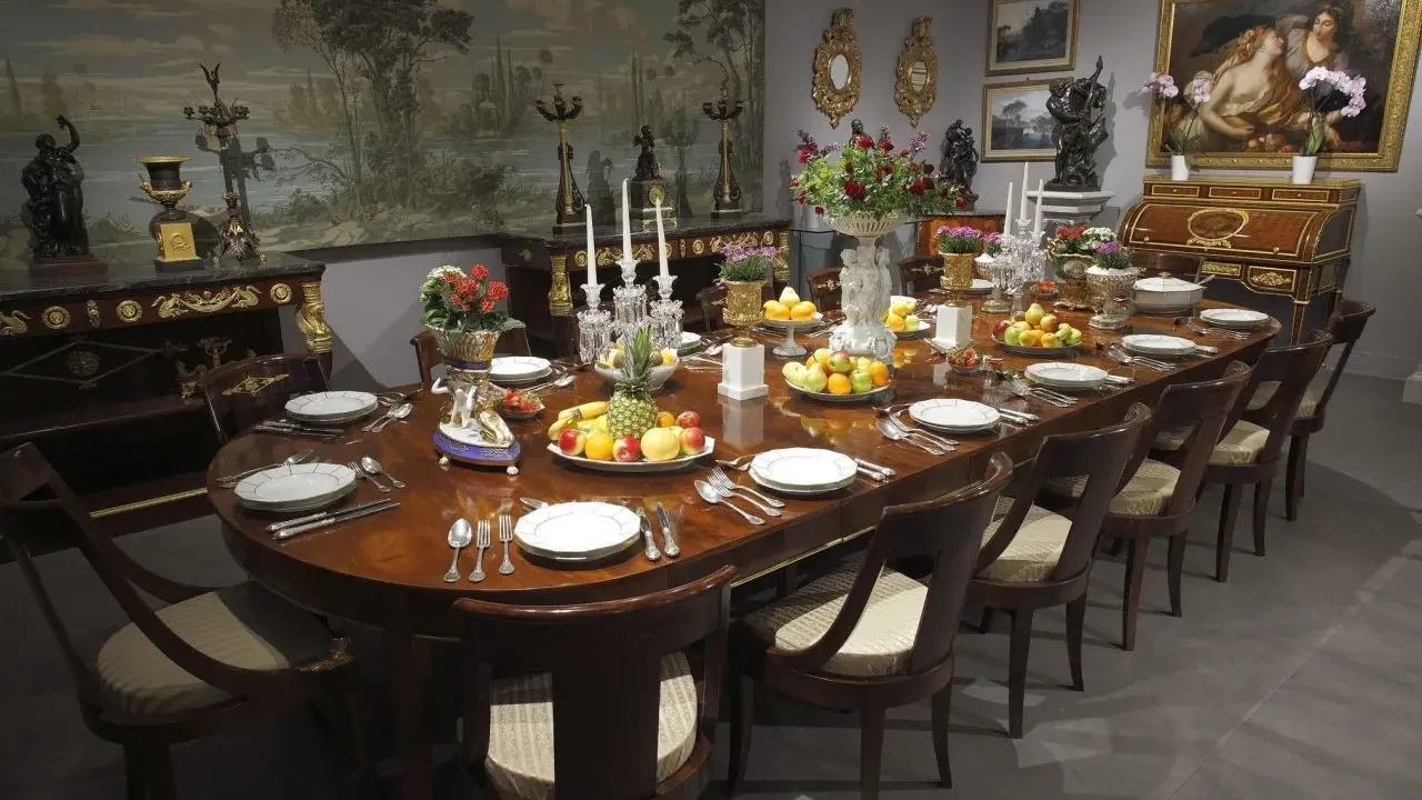 Table dressée dans un style directoire, avec fruits, fleurs et vaisselle raffinée. Le décor mural évoque un paysage champêtre.