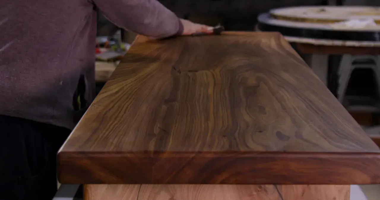 Main d'artisan polissant un plateau en bois de noyer, révélant la beauté du grain pour un traitement naturel bois parfait.