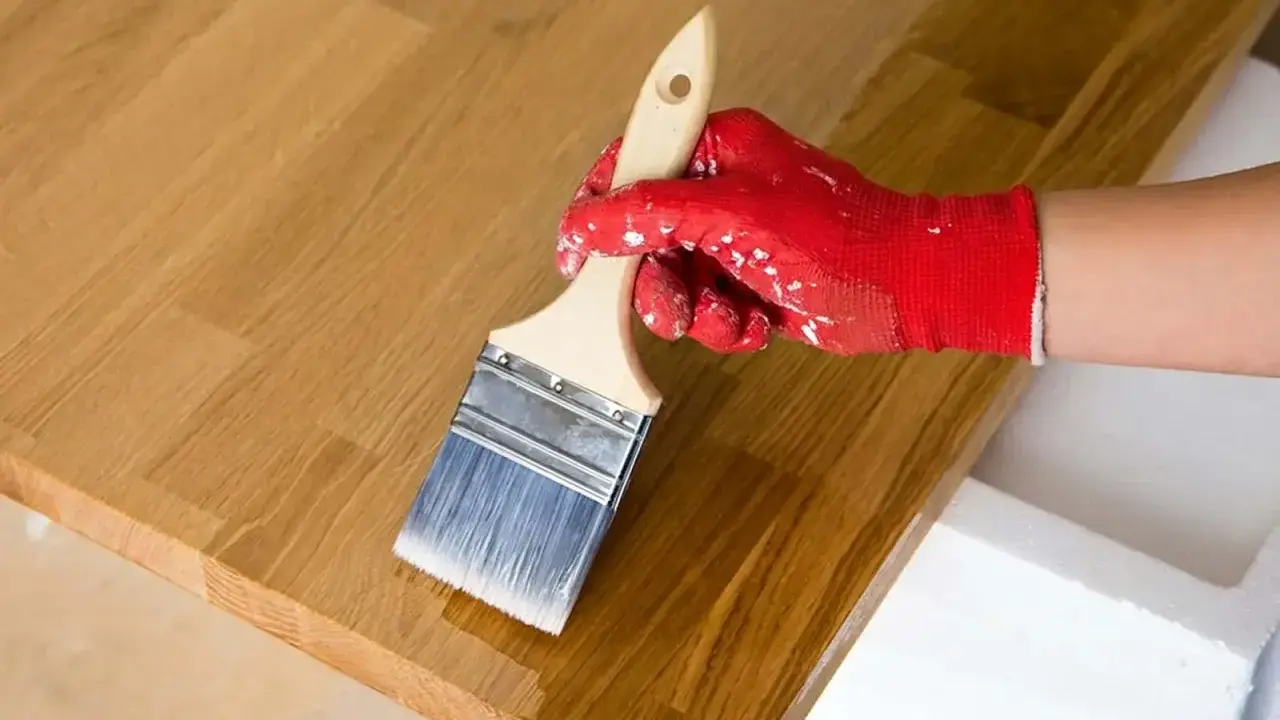 Application d'huile de lin sur un bois clair. La main gantée de rouge applique le produit pour protéger le bois, loin des insectes.