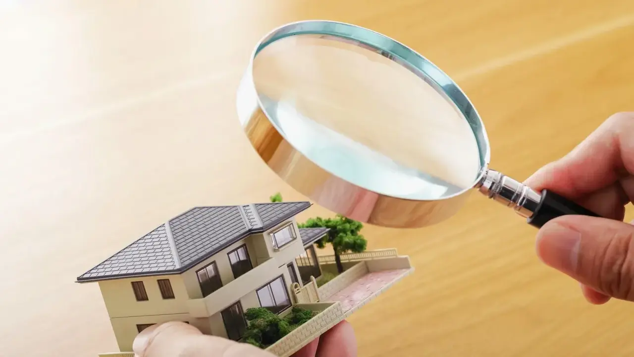 Main tenant examine un modèle de maison avec une loupe pour expertiser un tableau.