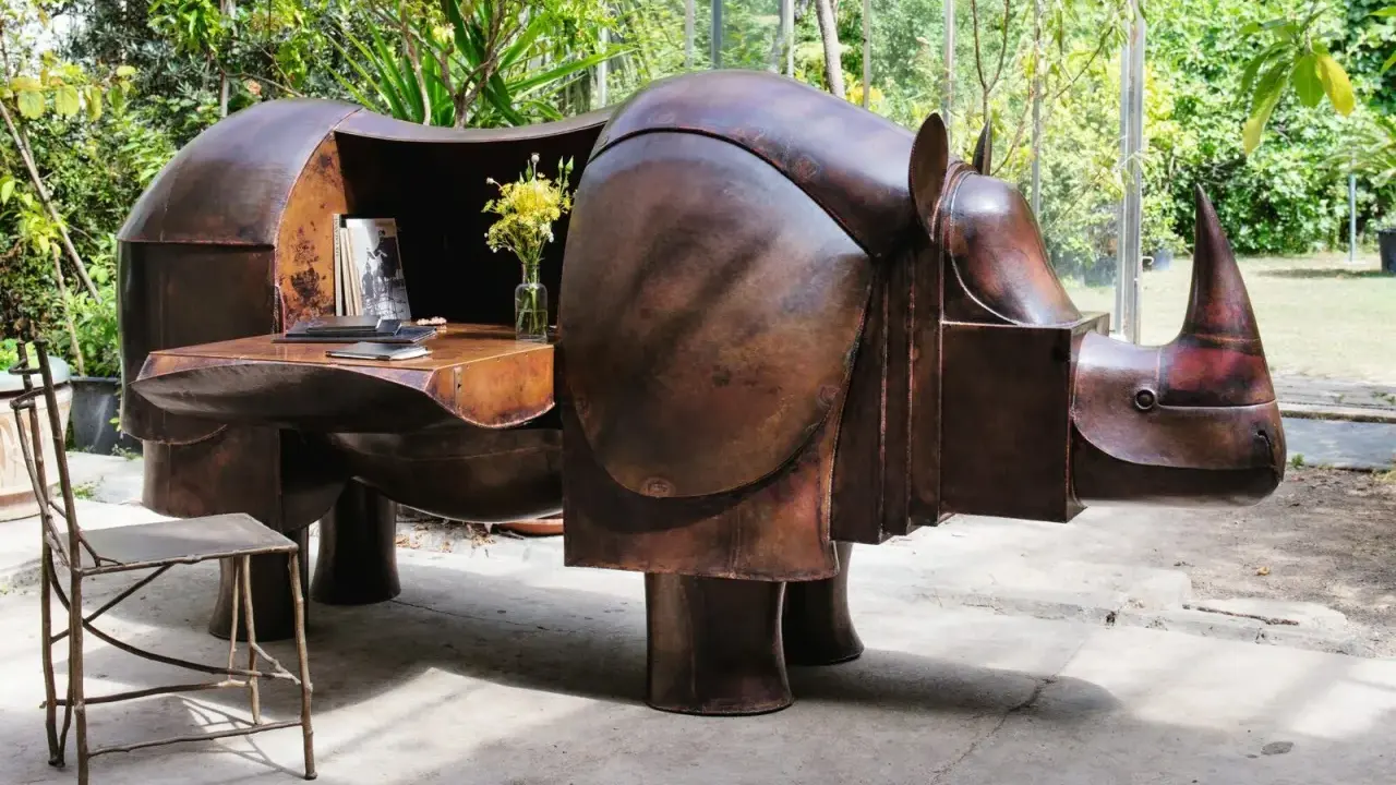 Étonnante sculpture lalanne en forme de rhinocéros, bureau fonctionnel en cuivre patiné, avec un vase de fleurs jaunes et une chaise en métal.