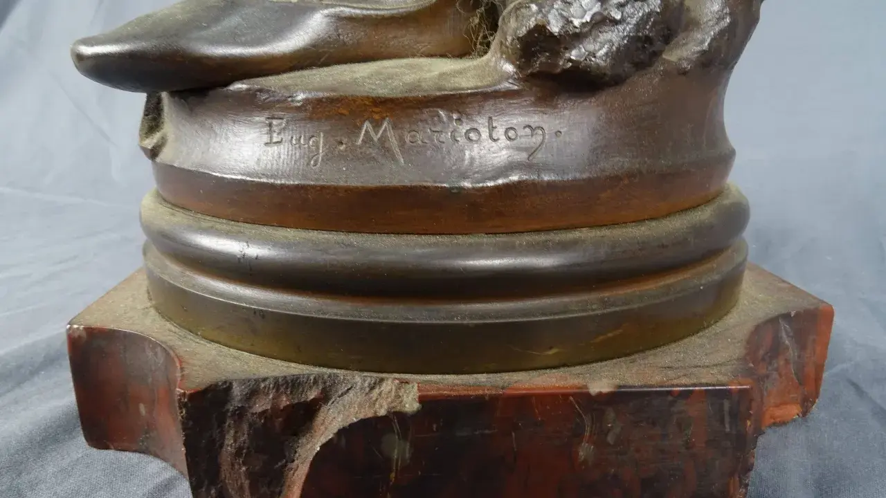Signature "Eug. Marioton" gravée sur la base d'une sculpture en bronze patiné, posée sur un socle en marbre rouge.