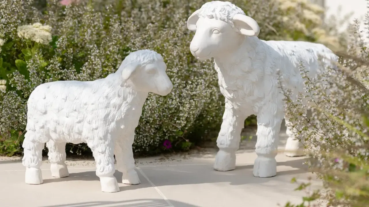Deux adorables agneaux en résine, œuvres de sculpteurs animaliers, semblent converser au milieu d'une végétation luxuriante.