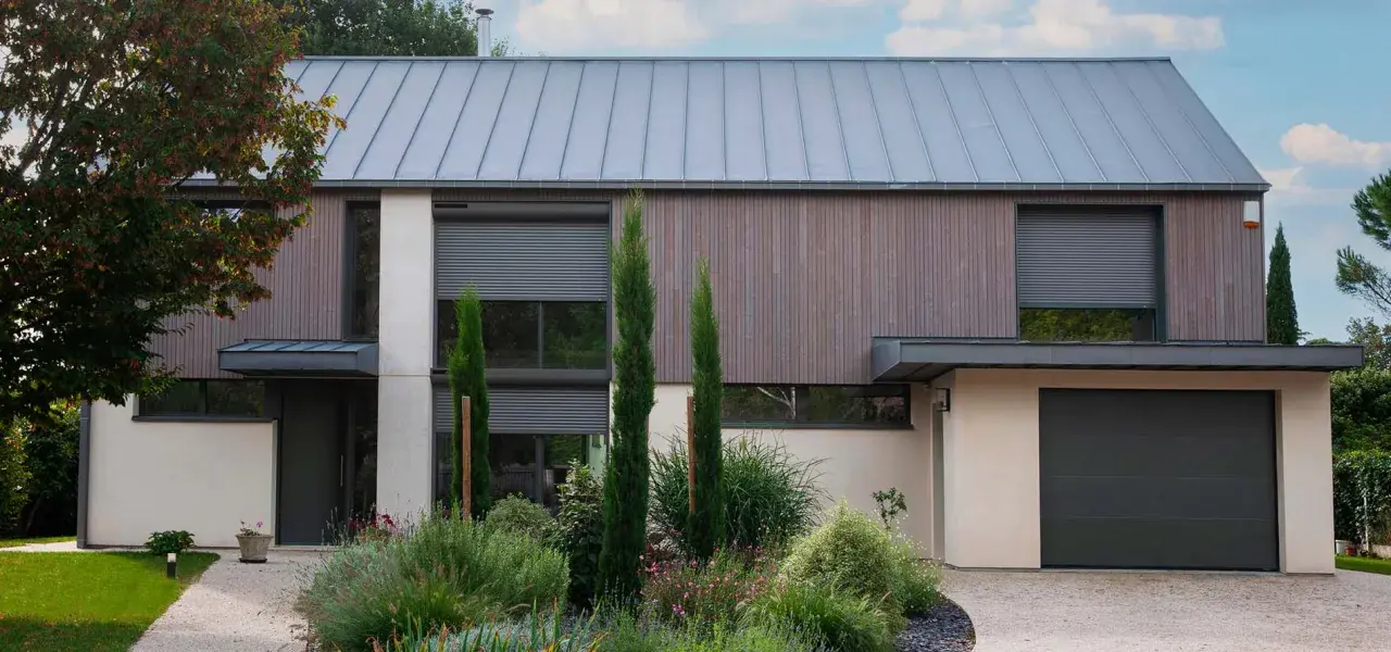 Façade moderne avec volet roulant maison ancienne, bois, pierre et jardin luxuriant.