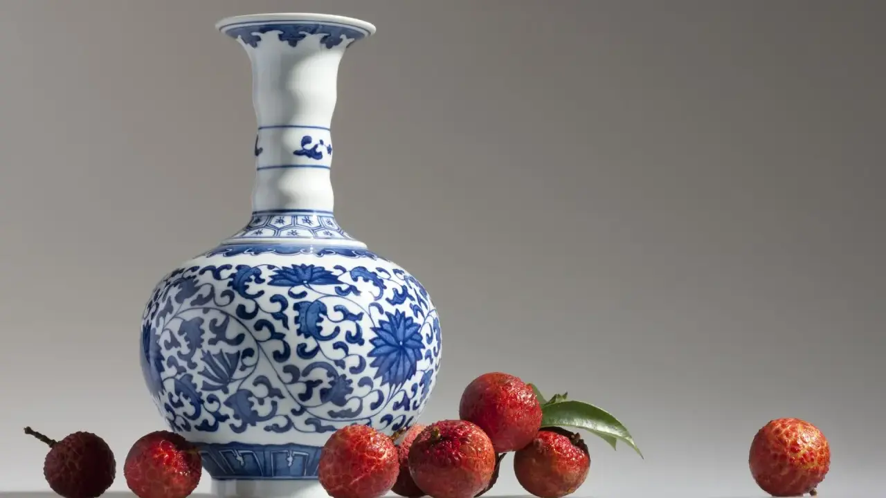 Un vase Satsuma bleu et blanc orné de motifs floraux, entouré de litchis rouges. Comment reconnaître un vase Satsuma ? Observez les détails.
