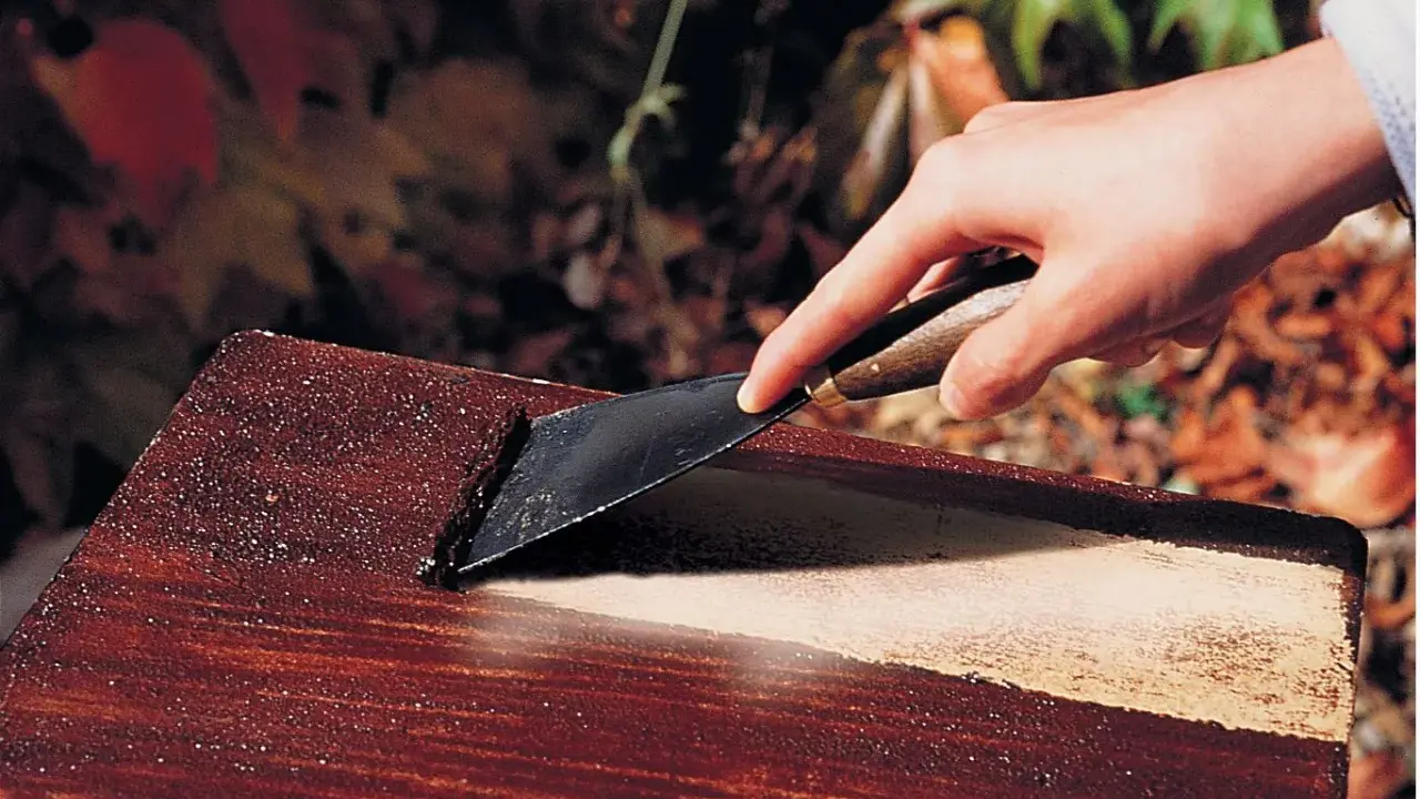 Main d'une personne utilisant un grattoir pour décaper peinture sur bois avec bicarbonate.