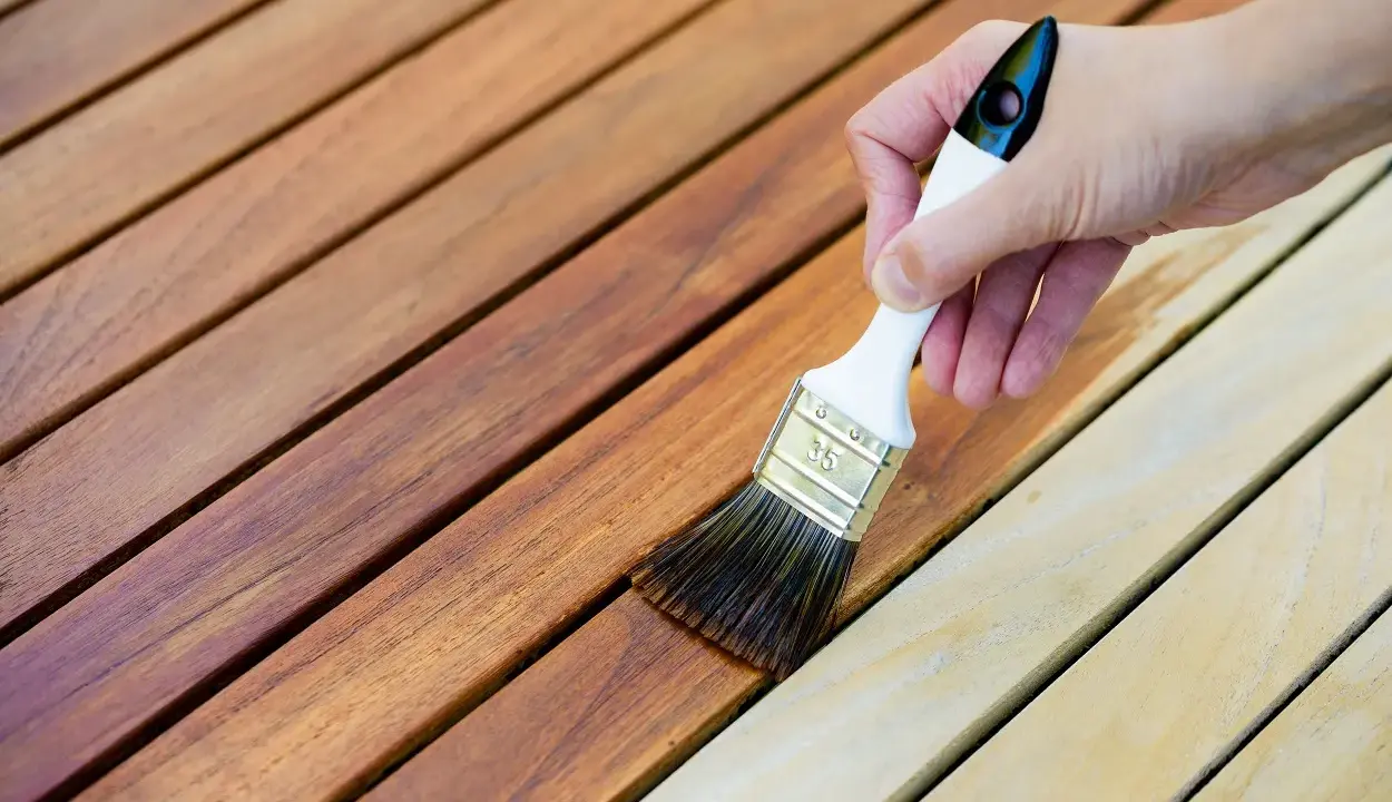 Application d'une lasure sur des lattes de bois. La différence entre lasure et peinture est visible : la lasure laisse le grain du bois apparent.