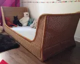 Lit en rotin tressé, style Louis Sognot, avec des peluches attendant patiemment dans un lit douillet.