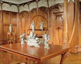 Intérieur Art Nouveau orné de boiseries sculptées, avec une table en bois et des sculptures, évoquant l'œuvre d'Alexandre Charpentier.