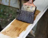 Pinceau appliquant une lasure sur une planche de bois clair, montrant la facilité de lasurer sans poncer pour une finition rapide et efficace.