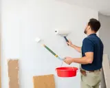 Un peintre applique une sous-couche blanche sur un mur avec deux rouleaux. Il tient un seau rouge. Peut-on mettre 2 couches de sous-couche pour un meilleur résultat ?