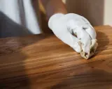 Main d'une personne portant un gant blanc, cirant un meuble en bois après décapage. La cire donne un éclat subtil au bois.