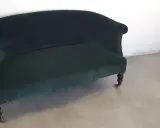 Banquette Napoléon III en velours vert profond, aux pieds sculptés et roulettes. Un meuble élégant pour un salon d'époque.