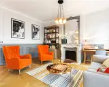 Salon aux fauteuils orange vif, cheminée ornée, et un jeu d'échecs sur table basse, évoquant un mouvement baroque moderne.