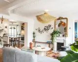 Salon au style classique revisité, avec un canapé gris, un tapis coloré, une cheminée ornée et des plantes luxuriantes.