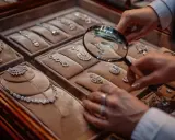Main d'un expert examinant des colliers et pendentifs en diamants avec une loupe, témoignant d'une expertise bijoux.