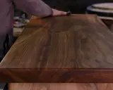 Main d'artisan polissant un plateau en bois de noyer, révélant la beauté du grain pour un traitement naturel bois parfait.