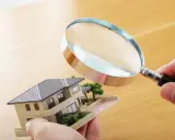 Main tenant examine un modèle de maison avec une loupe pour expertiser un tableau.