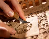 Main d'artisan sculptant un motif floral sur un meuble en bois, étape clé pour savoir comment nettoyer un meuble en marqueterie.