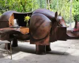 Étonnante sculpture lalanne en forme de rhinocéros, bureau fonctionnel en cuivre patiné, avec un vase de fleurs jaunes et une chaise en métal.
