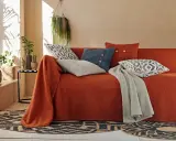 Un canapé ancien relooké en orange vif, orné de coussins graphiques et d'une couverture grise. Une touche bohème moderne.