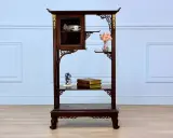 Étagère en bois sombre ornée de motifs dorés, rappelant le style de Gabriel Viardot. Elle présente des tasses dans une vitrine, des livres et des fleurs.