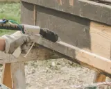Main tenant en décapeur thermique pour enlever peinture sur bois. Le bois brut apparaît sous la couche sombre.