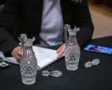 Une personne écrit sur un carnet, entourée de flacons en cristal. Une folle enchère se prépare pour ces objets précieux.