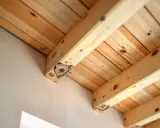 Structure en bois clair, avec des poutres et des planches. On aperçoit un champignon bois extérieur sur une poutre, signe d'une construction ancienne.