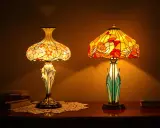 Deux lampes art nouveau Gallé aux abat-jour colorés, l'une ornée de fleurs, l'autre de motifs floraux, éclairent une table en bois.