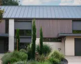 Façade moderne avec volet roulant maison ancienne, bois, pierre et jardin luxuriant.