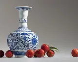 Un vase Satsuma bleu et blanc orné de motifs floraux, entouré de litchis rouges. Comment reconnaître un vase Satsuma ? Observez les détails.