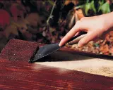 Main d'une personne utilisant un grattoir pour décaper peinture sur bois avec bicarbonate.