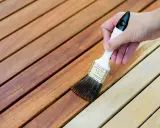 Application d'une lasure sur des lattes de bois. La différence entre lasure et peinture est visible : la lasure laisse le grain du bois apparent.