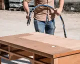 Un homme utilise un appareil pour poncer ou décaper un bureau en bois, révélant une surface plus claire.