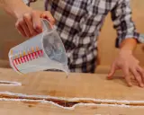 Application d'une résine pour comment empêcher le bois de gonfler. Un artisan verse un liquide d'un gobelet gradué sur une planche de bois.
