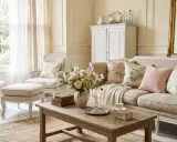 Salon au style antique, avec canapé et fauteuils en lin, coussins fleuris, table basse en bois brut et miroir doré.