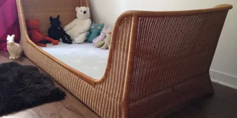 Lit en rotin tressé, style Louis Sognot, avec des peluches attendant patiemment dans un lit douillet.