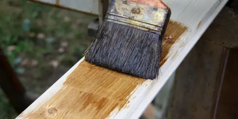Pinceau appliquant une lasure sur une planche de bois clair, montrant la facilité de lasurer sans poncer pour une finition rapide et efficace.