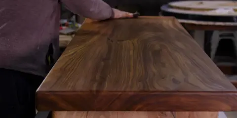 Main d'artisan polissant un plateau en bois de noyer, révélant la beauté du grain pour un traitement naturel bois parfait.